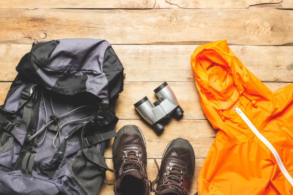 Equipo básico para senderismo con mochila, botas de montaña, prismáticos y chaqueta impermeable preparados antes de la ruta